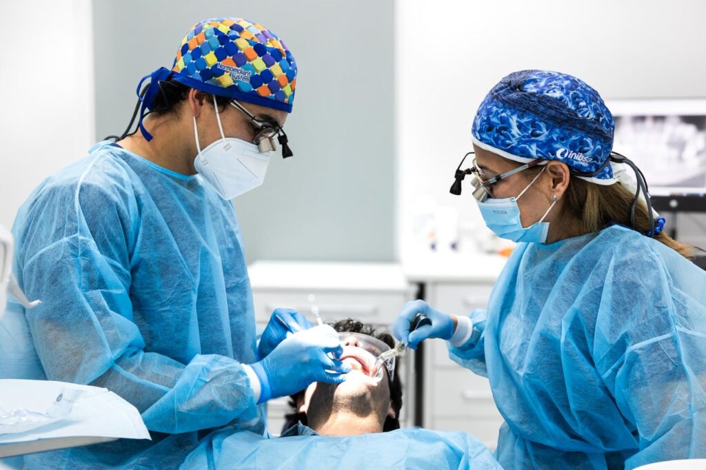 dentistas realizando procedimiento dental a paciente con mascarillas y batas azules