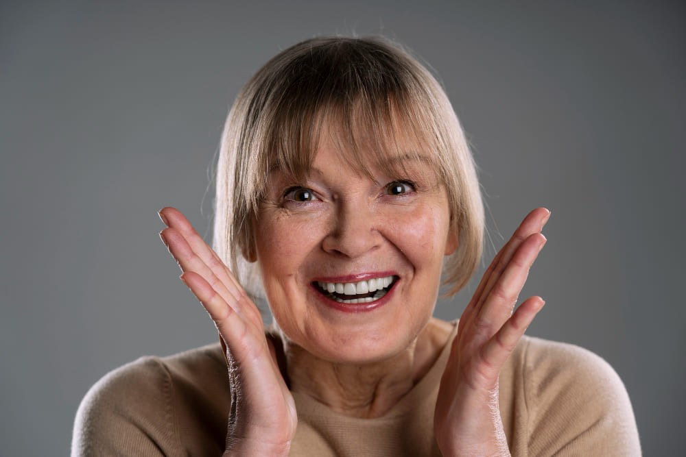 mujer madura sonriendo con expresion de sorpresa y alegria dientes visibles en estudio